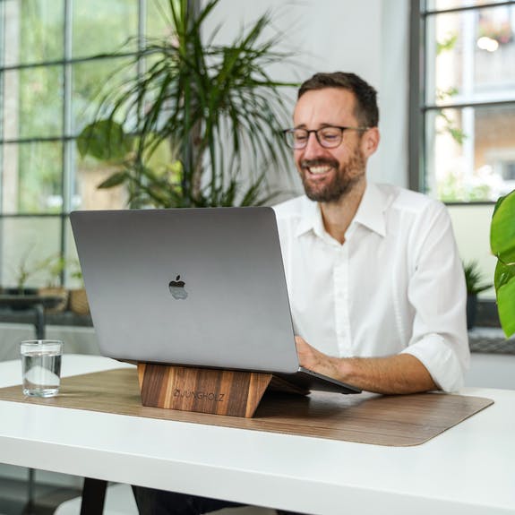 male working at desk with MacBook Pro on a walnut laptop stand