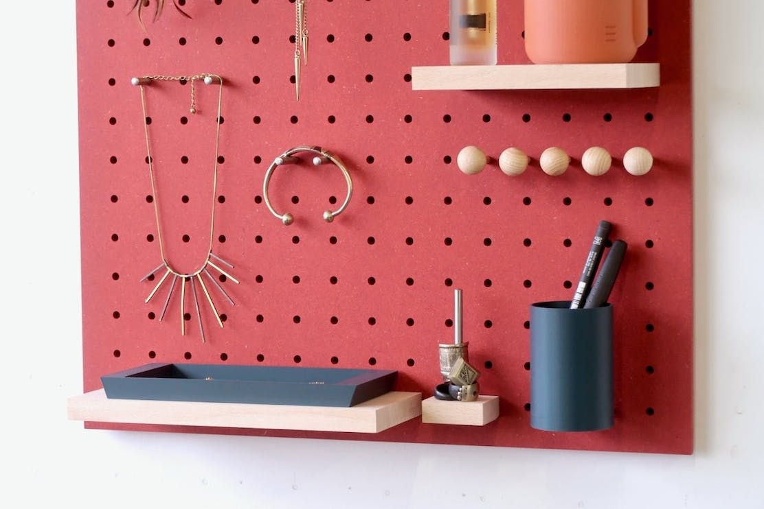 close up of red pegboard system showing stationary pot and a wooden shelf