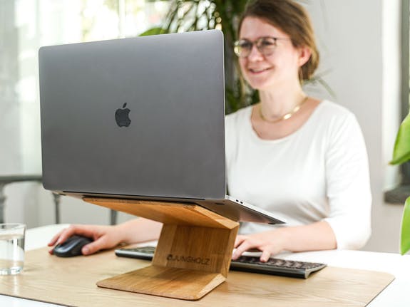 female working at a desk, using a MacBook on an oak laptop riser stand