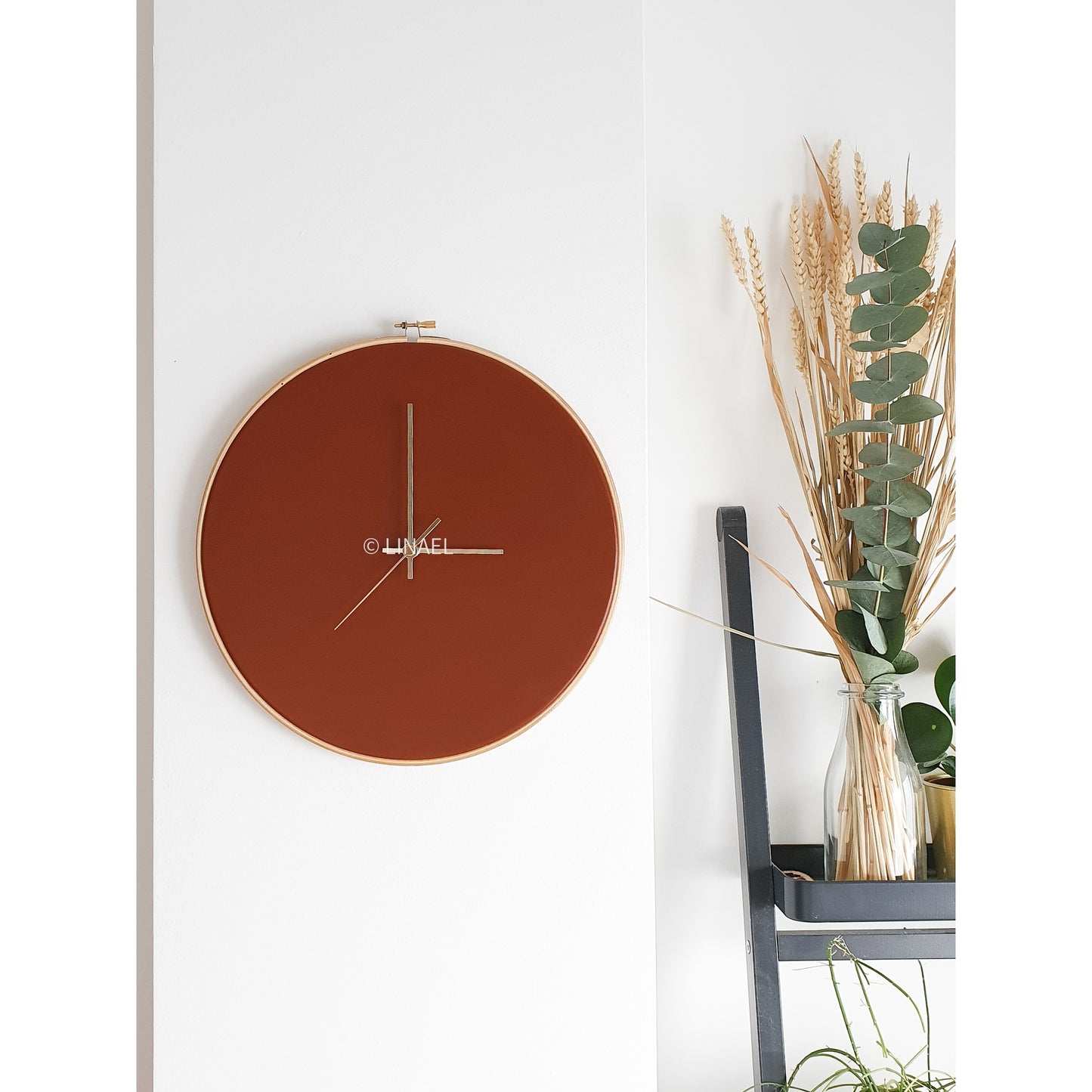 lineal brown leather wall clock next to a houseplant