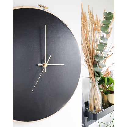 black lineal wall clock on white wall next to plant