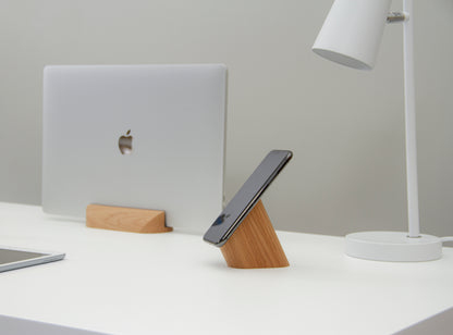 oak mobile phone stand next to a MacBook Pro on an office desk